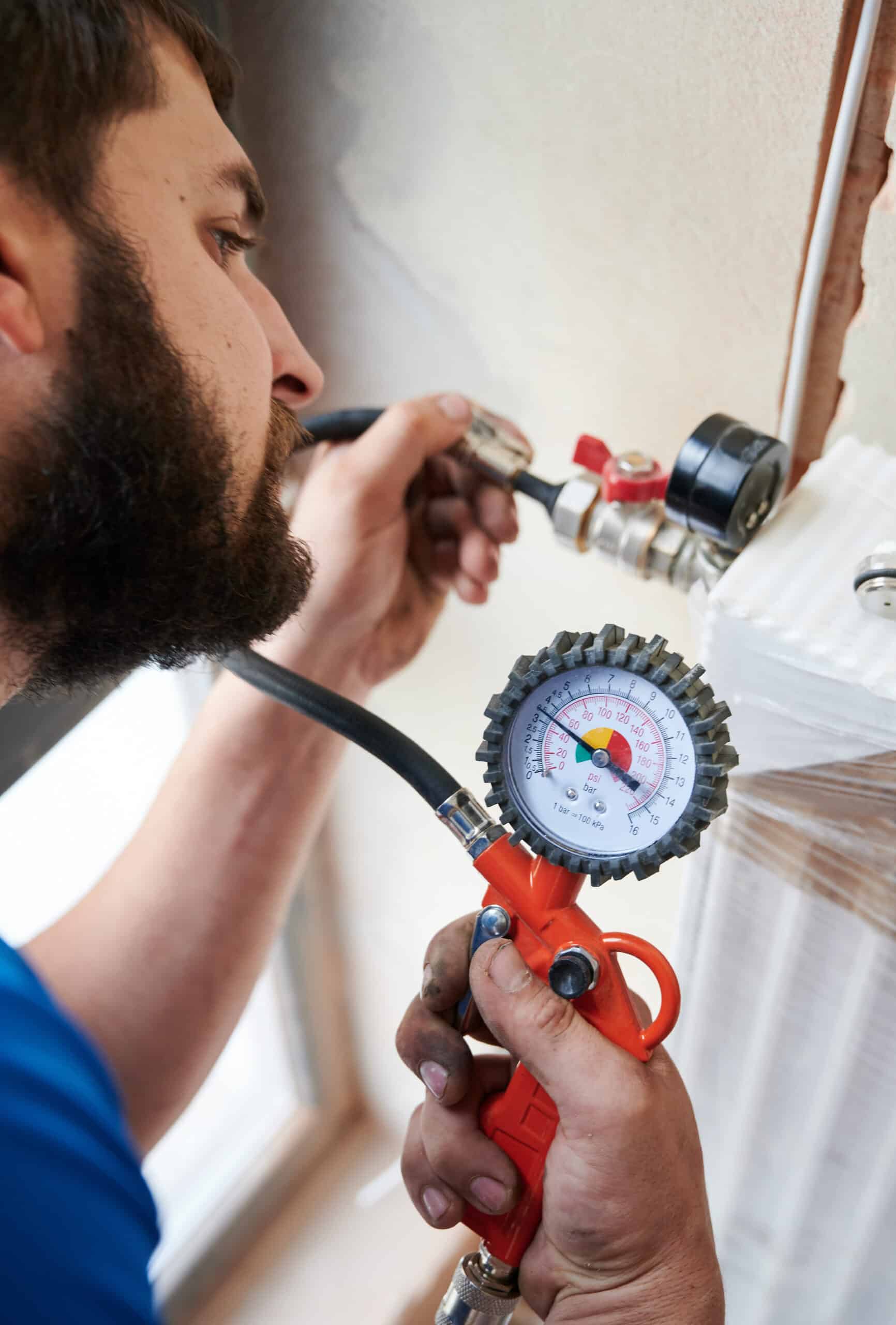 Close up of bearded man filling pipes with pressurized air to inspect for leaks in new installation. Worker using manometer, checking gas tightness of heating system. Concept of gas tightness testing.
