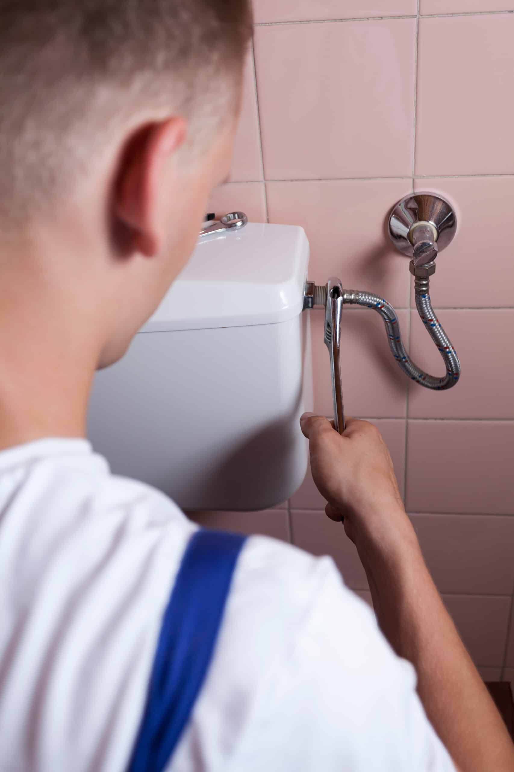 Back view of a plumber fixing a flush toilet